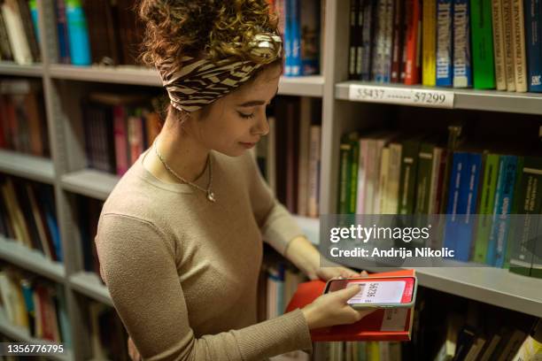 female student scanning book code in the library - openbare bibliotheek stockfoto's en -beelden