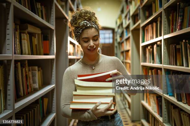 smiling student holding books at library - student reading book stockfoto's en -beelden