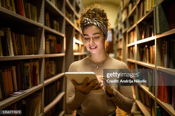 young female student using tablet for reading in the library - ereader stock pictures, royalty-free photos & images