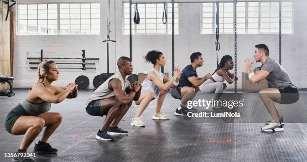 shot of a group of young people exercising under the watchful eye of their trainer at the gym - crouch stock pictures, royalty-free photos & images