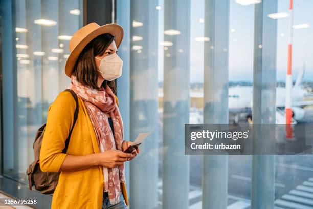 young woman with mask looking the airport runway from the window - repatriation stockfoto's en -beelden