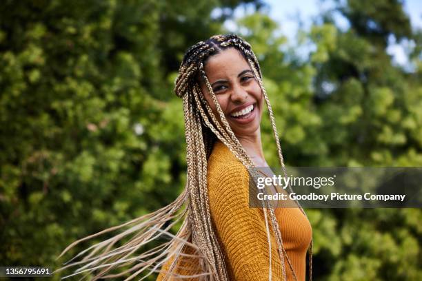 laughing young woman twirling her long braided hair outside in summer - plait stockfoto's en -beelden