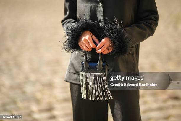 Angela Gonzalez wears a black satin silk shirt with feathers on the borders, matching black satin silk pants with feathers on the ankle, a black...