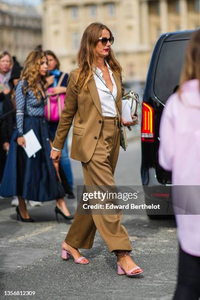 Guest wears brown sunglasses, gold chain pendant necklaces, a white shirt, a brown blazer jacket, matching brown large suit pants, a khaki and gray...