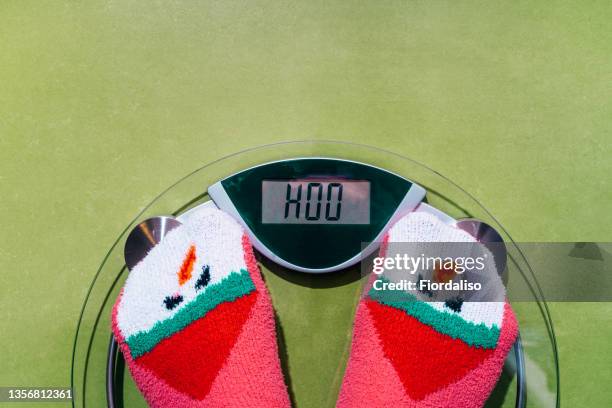 woman standing on the scales in christmas fun red green socks with snowman background. the problem of excess weight gained during the holiday new year - funny fat women stockfoto's en -beelden