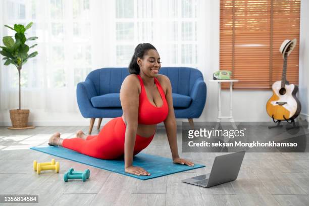 video lesson. overweight young woman repeating exercises while watching online workout session - beautiful fat ladies stock-fotos und bilder