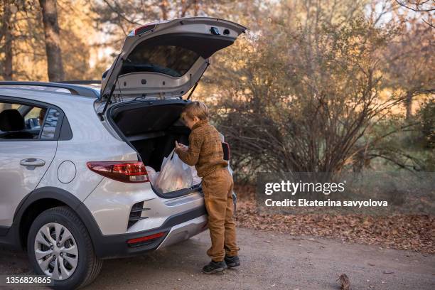 the boy puts shopping bags in the car and closes the trunk. - car in driveway stock-fotos und bilder