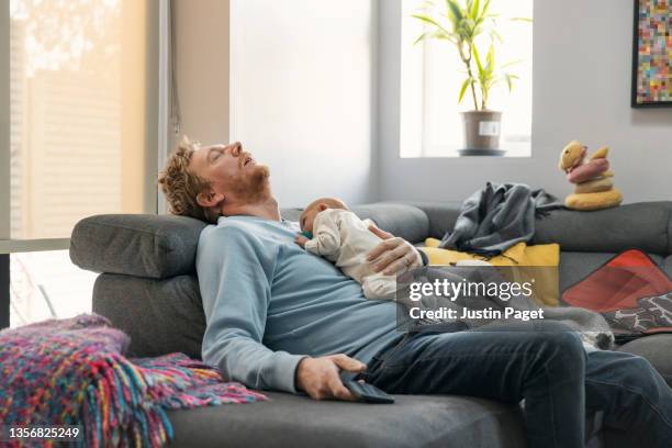 exhausted father lies asleep on the sofa holding his baby girl - cansado fotografías e imágenes de stock