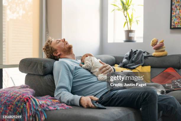 exhausted father lies asleep on the sofa holding his baby girl - man sleeping stock pictures, royalty-free photos & images