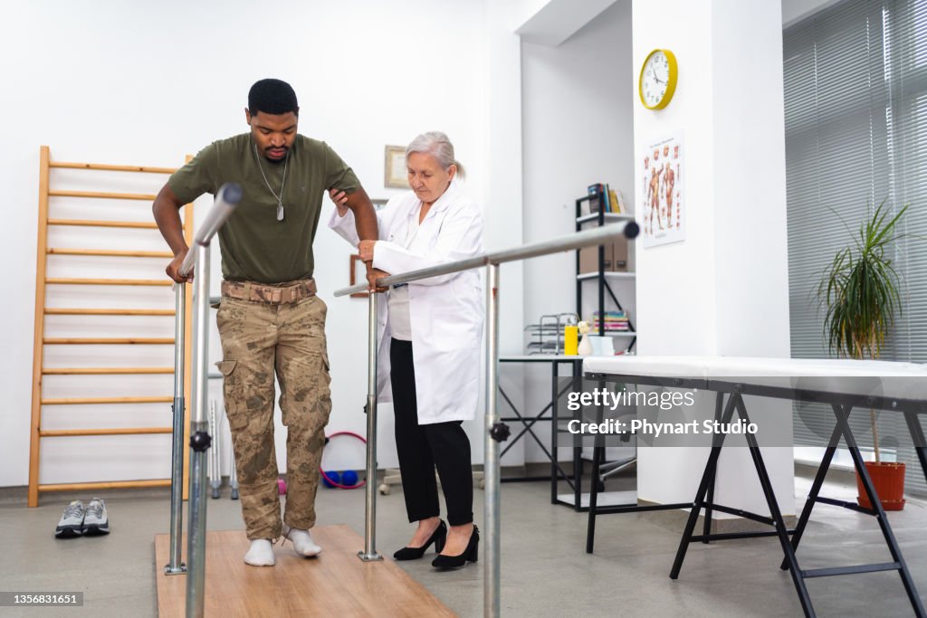 Young military soldier uses parallel bars in a rehab center.