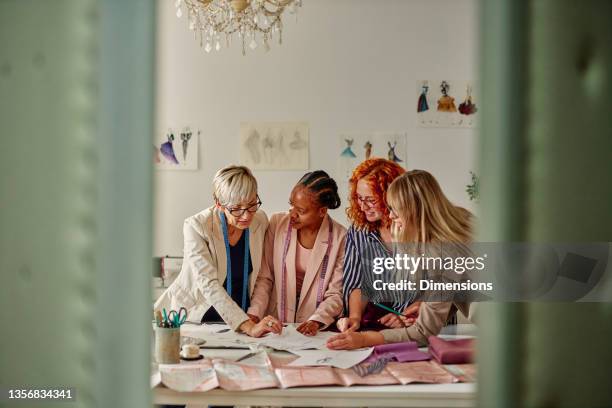 fashion designers in a meeting standing reviewing a sketches - textile industry imagens e fotografias de stock