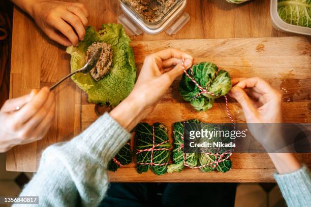 hands of women making stuffed christmas cabbage rolls on kitchen table - cabbage roll stock pictures, royalty-free photos & images