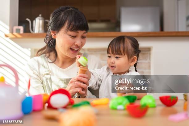 mutter und ihre kleine tochter spielen mit spielzeuggemüse und küchenutensilien im wohnzimmer zu hause - baby spielt mit essen stock-fotos und bilder