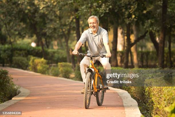 senior man riding bicycle at park - adult riding bike through park stock pictures, royalty-free photos & images