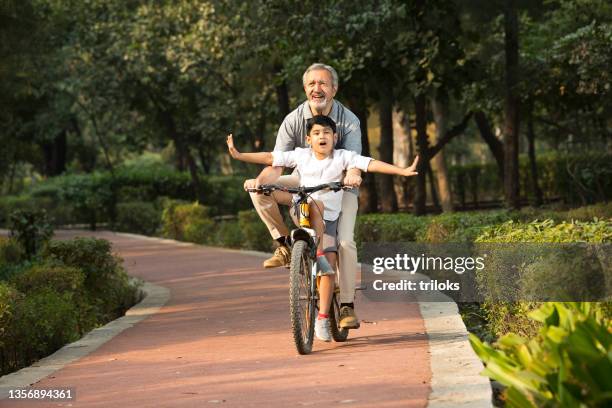 grandfather with grandson riding bicycle at park - indian sports and fitness stock pictures, royalty-free photos & images