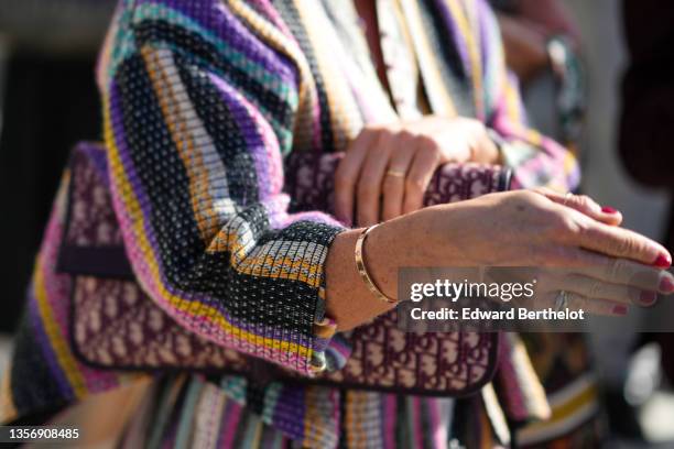 Guest wears a black / orange / silver / pink / purple / green striped jacket, a gold Love bracelet from Cartier, a burgundy and beige Dior Oblique...