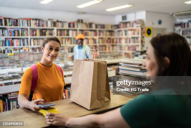 teenager-mädchen, das in einem secondhand-laden bezahlt - buchhandlung stock-fotos und bilder