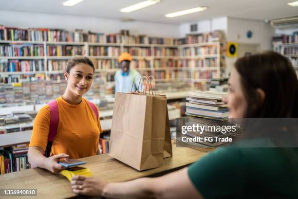 teenager-mädchen, das in einem secondhand-laden bezahlt - bookstore stock-fotos und bilder