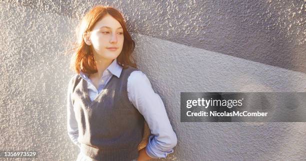 female teenager looking away in student wardrobe lit sideways by sunset - sweater vest stock pictures, royalty-free photos & images