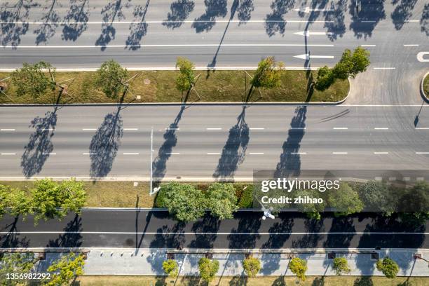 a multi-lane asphalt road overlooking the city, with greenery and tree shadows - mittelstreifen stock-fotos und bilder