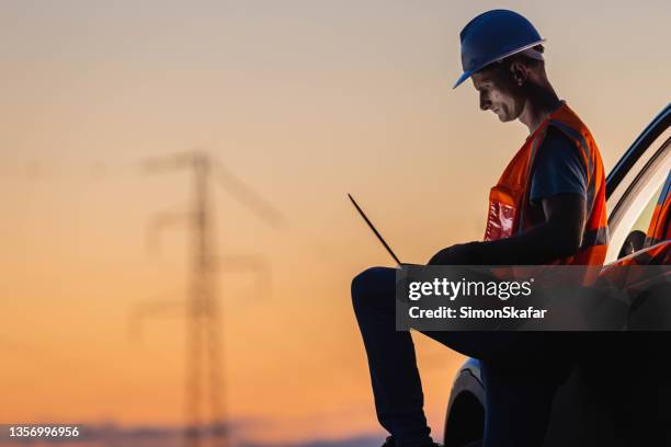 ingenieur, der an einem gerät mit einem hochspannungspol im hintergrund arbeitet - gas plant sunset stock-fotos und bilder