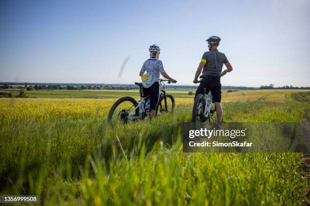 sporty couple cycling on electric mountain bikes in rural environment - elektrische fiets stockfoto's en -beelden