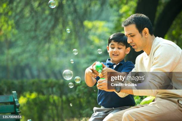 père et fils jouant avec un pistolet à bulles au parc - daily life in india photos et images de collection