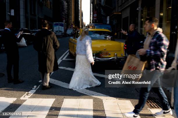 People walk past a woman in a wedding dress taking wedding photos near an old fashioned yellow cab in Midtown Manhattan on December 03, 2021 in New...