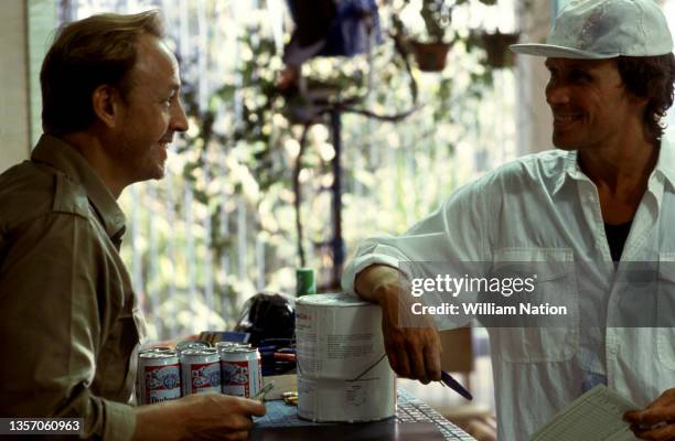 American actor Frederic Forrest talks with American film and stage actor Peter Weller as they film a scene during the 1989 drama film "Cat Chaser"...