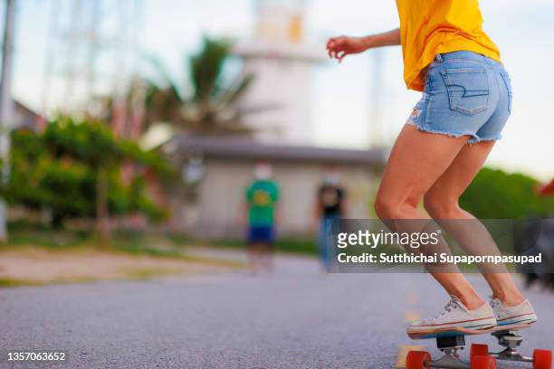 happy asian female playing surf skate on the road. - woman longboard stock-fotos und bilder
