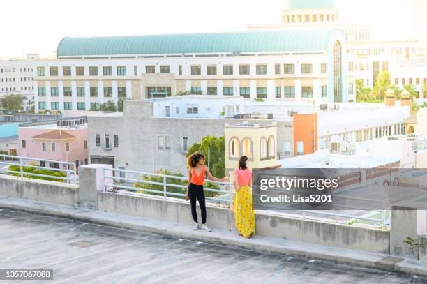 two cool young women in vibrant clothing hang out together on an urban summer rooftop overlooking the city of west palm beach florida - west palm beach stock pictures, royalty-free photos & images