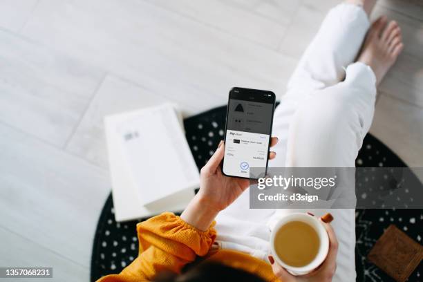 overhead view of young asian woman relaxing at home, shopping online with smartphone and making payment online with credit card. lifestyle and technology. contactless payment. comfortable and fast shopping experience - online shopping foto e immagini stock
