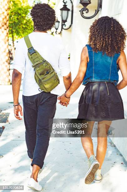 cute black young couple holding hands and walking on a city sidewalk seen from behind - crossbody bag stock pictures, royalty-free photos & images