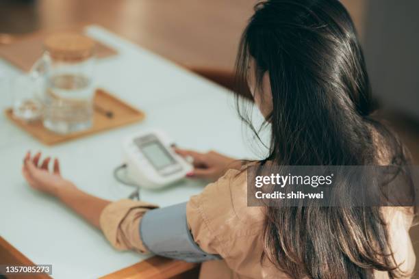 adult woman measuring blood pressure at home - cardiovascular disease stockfoto's en -beelden