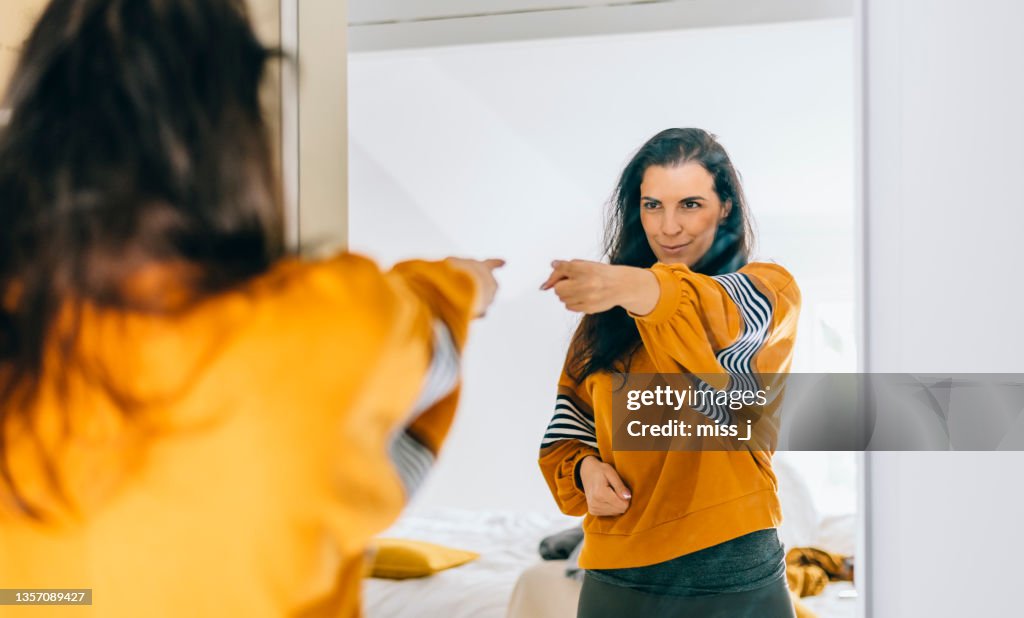 Self confident single woman pointing finger at her reflection in mirror, dancing and felling good