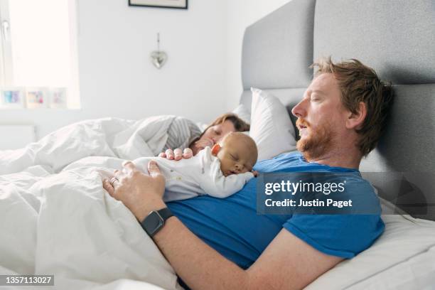 newborn baby asleep on father's chest whilst the mother sleeps in background - sleeping baby stock pictures, royalty-free photos & images