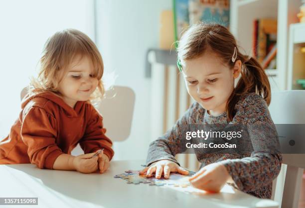 hermanas sonrientes jugando en la habitación de casa con rompecabezas - coco girls fotografías e imágenes de stock