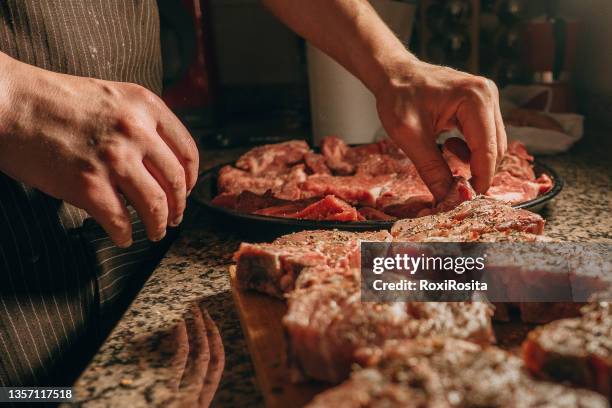 close-up of two hands seasoning pork cuts on a wooden board - argentina steak fotografías e imágenes de stock