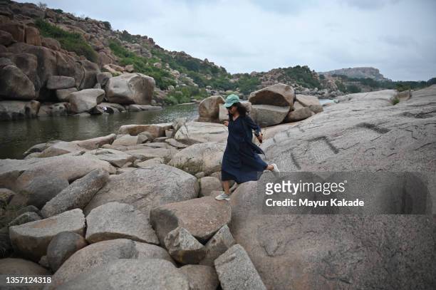 woman walking in the boulders alongside a river at hampi, karnataka - humpi stock pictures, royalty-free photos & images