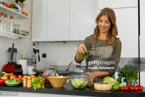 frau, die eine handvoll rucola zu einem salat hinzufügt, den sie zubereitet - rucola stock-fotos und bilder