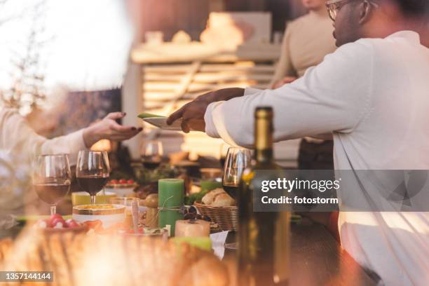 friends setting up plates on a dining table before eating main dish during christmas lunch - dinner party stock pictures, royalty-free photos & images