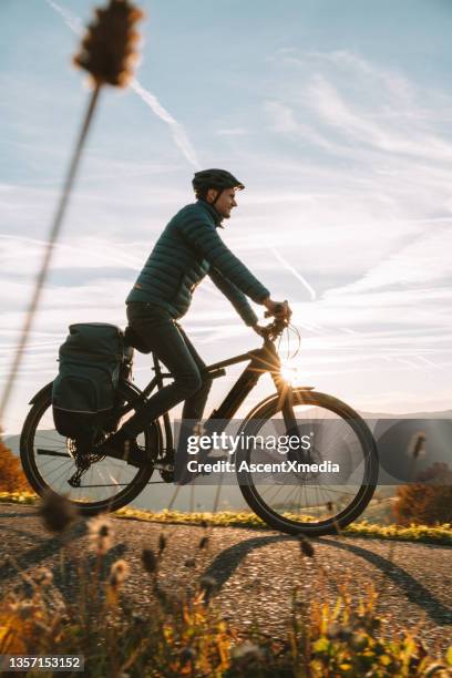 young man rides e-mountain bike down road - ebike stock pictures, royalty-free photos & images