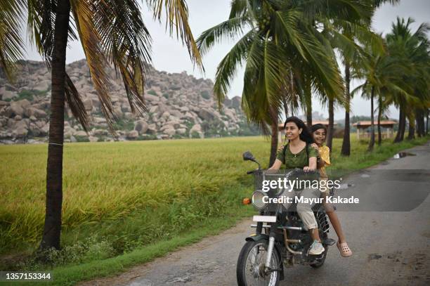 mother and daughter riding a two wheeler on beautiful rural road - indian family vacation stock pictures, royalty-free photos & images