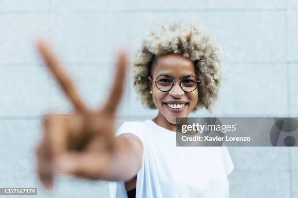 happy young latina woman showing peace gesture in front of yellow wall - free sign imagens e fotografias de stock