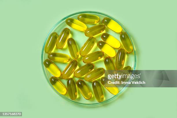 petri dish with the  fish oil capsules with omega 3, vitamin d on pastel green color background. - fish oil stockfoto's en -beelden