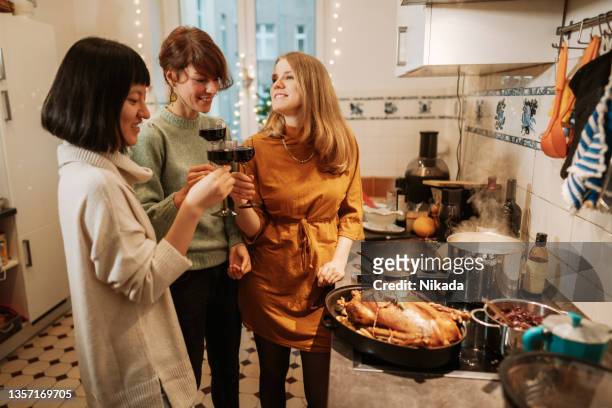 three women drinking wine while preparing christmas dinner at home - christmas drinks stockfoto's en -beelden