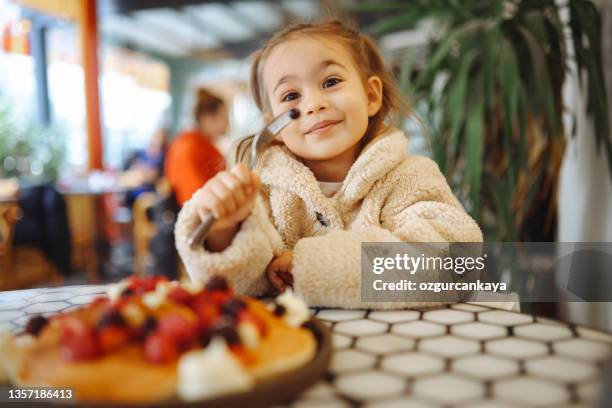 little girl eating breakfast crepes with fruits - children restaurant stock pictures, royalty-free photos & images