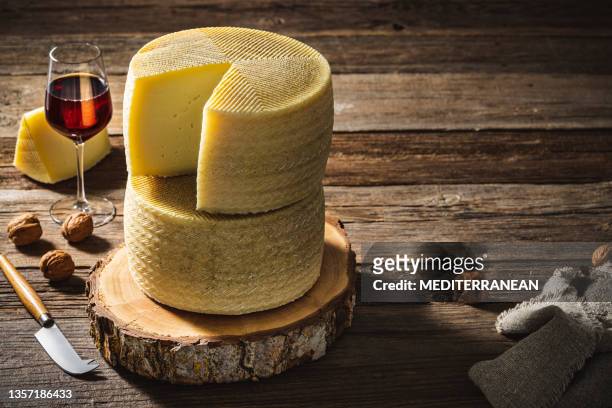 queso manchego rueda de queso 2 piezas y copa de vino tinto sobre rústico - queso manchego fotografías e imágenes de stock