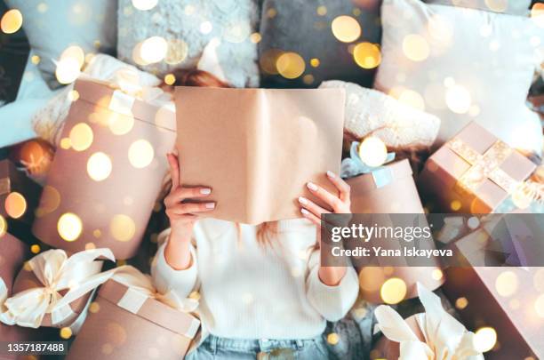 beautiful woman is reading a book, laying between gift boxes, enjoying christmas sale offers - sortie de livre photos et images de collection