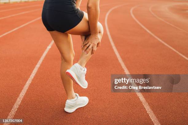 running injury, health problems in sport. hands holding spasmed calf or achilles muscle on sports track - female muscular calves fotografías e imágenes de stock